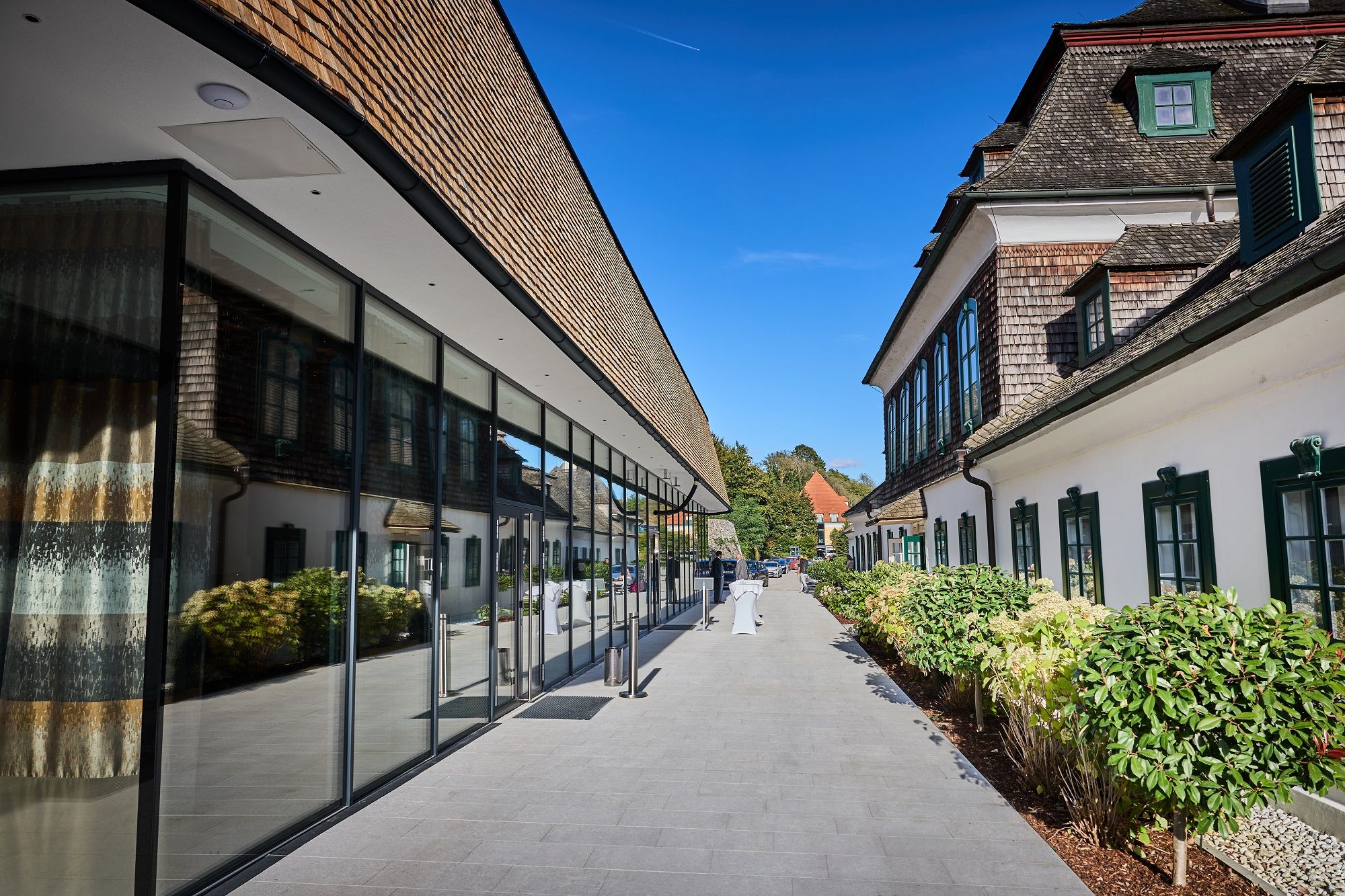 Moderne Glasfassade neben historischem Gebäude mit grünem Fensterrahmen, blauer Himmel.