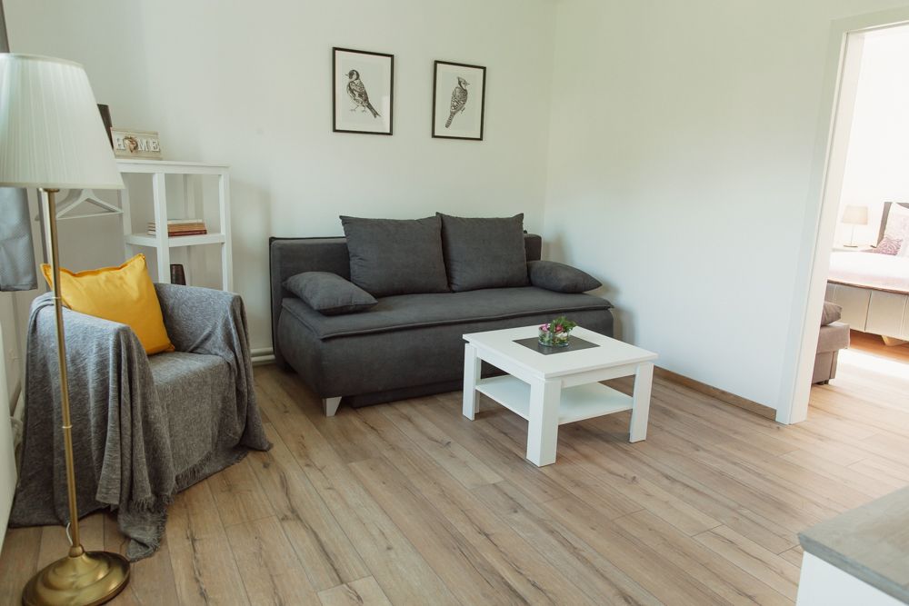 Modernes Wohnzimmer mit grauem Sofa, Sessel, weißem Couchtisch und Holzboden.
