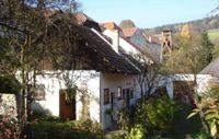 Ein ländliches Gebäude mit weißen Wänden und roten Ziegeldächern, umgeben von Bäumen und Büschen.
