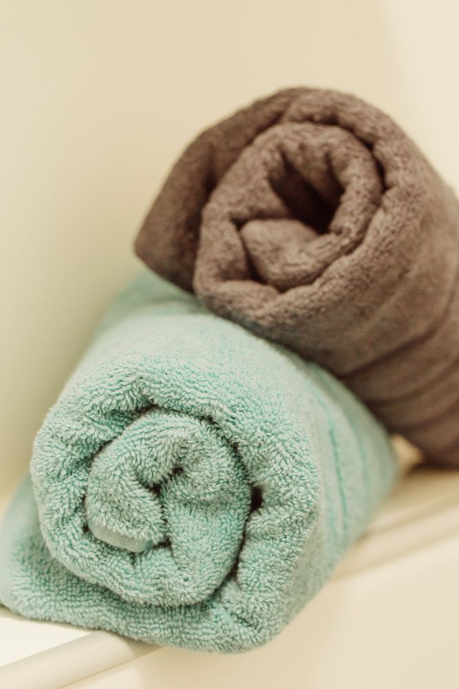 Zwei aufgerollte Handtücher, eines in Türkis und eines in Braun, liegen auf einem Regal.