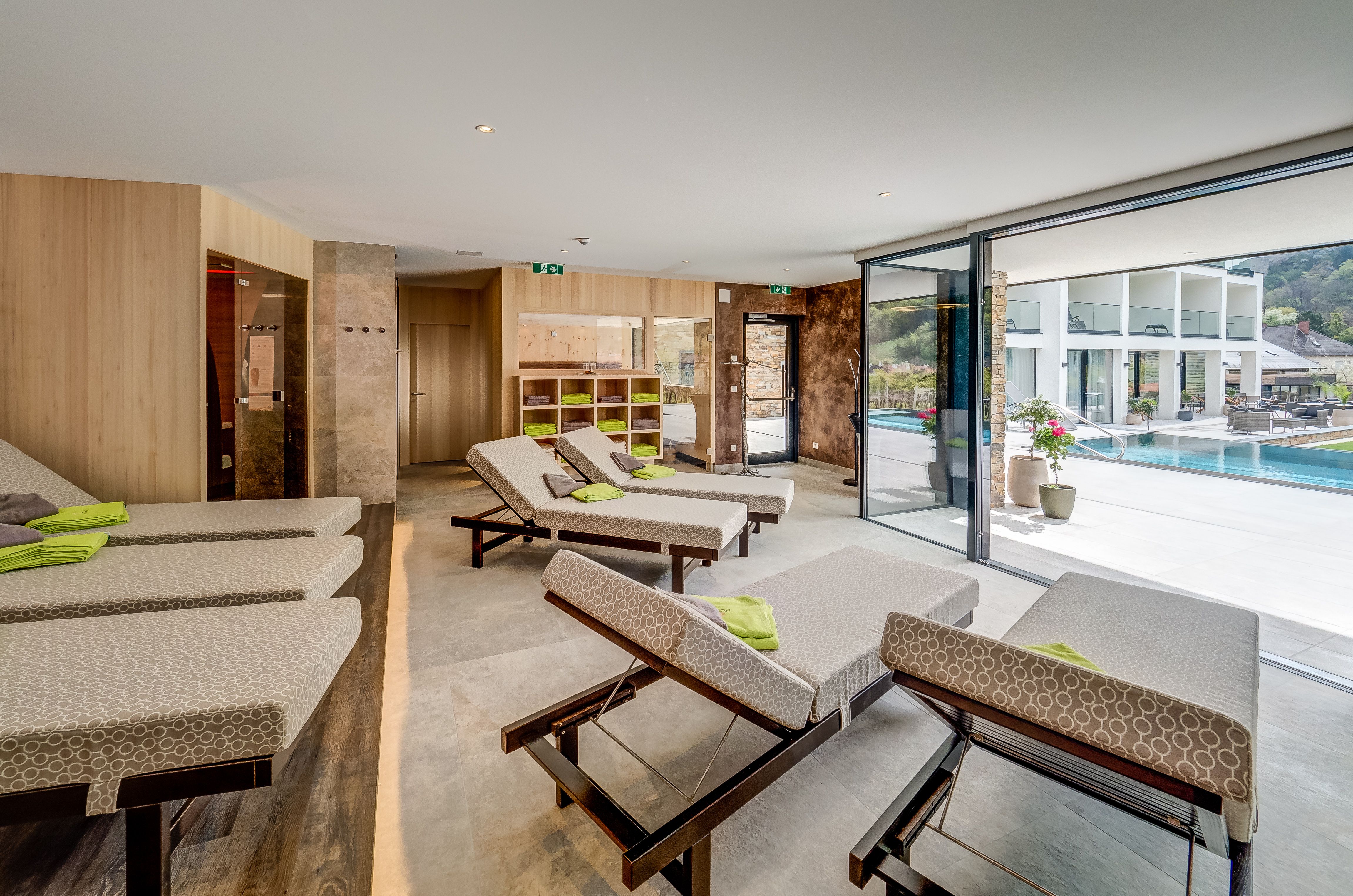 Moderner Ruhebereich mit Liegen und Blick auf einen Pool durch große Fenster.
