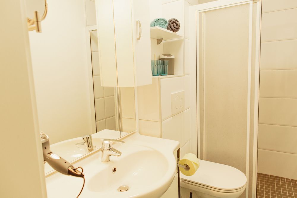 Kleines Badezimmer mit Waschbecken, Spiegel, Dusche und Toilette.