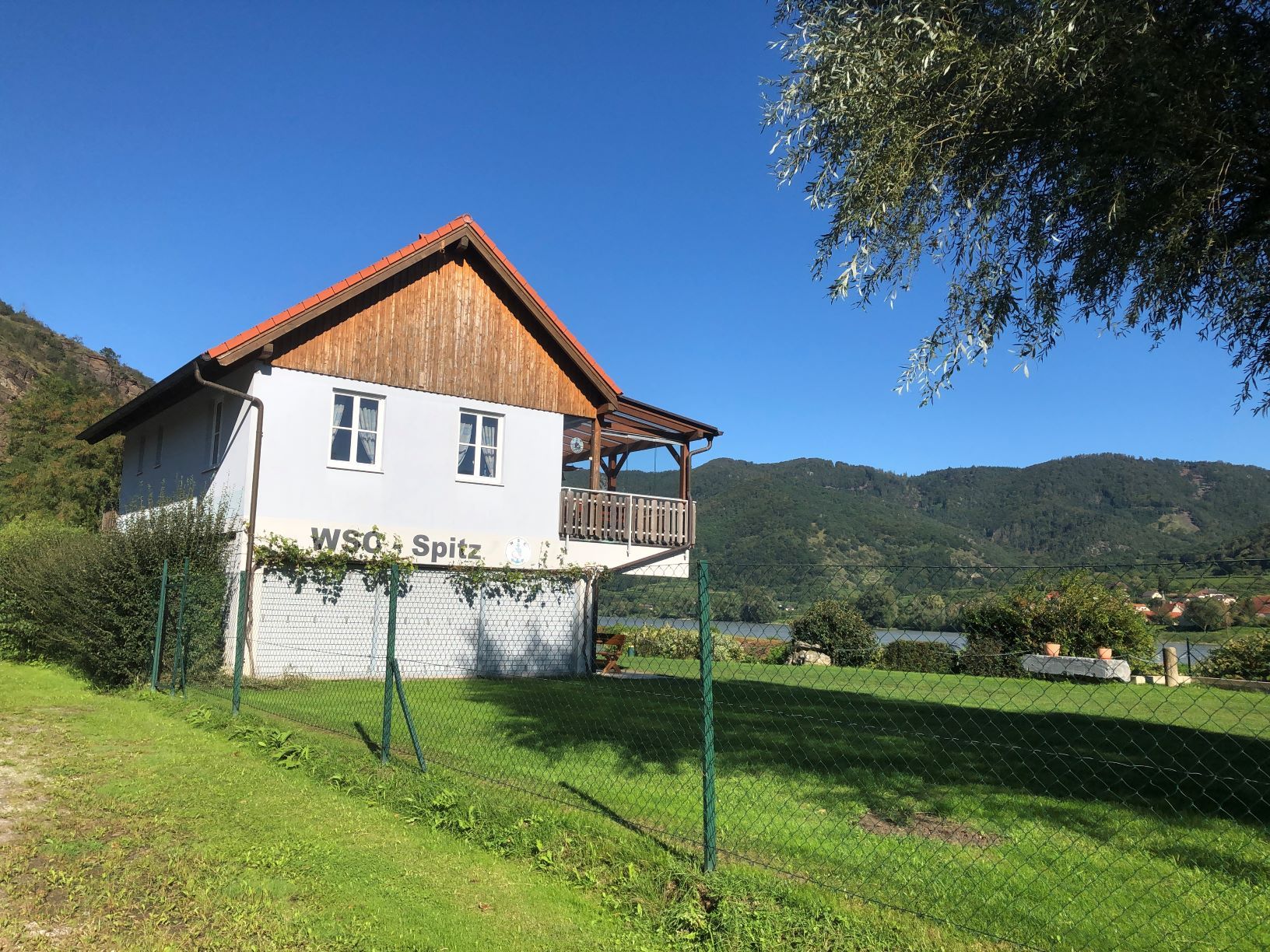 Ein Clubhaus mit der Aufschrift 'WSC Spitz' vor einer Berglandschaft.