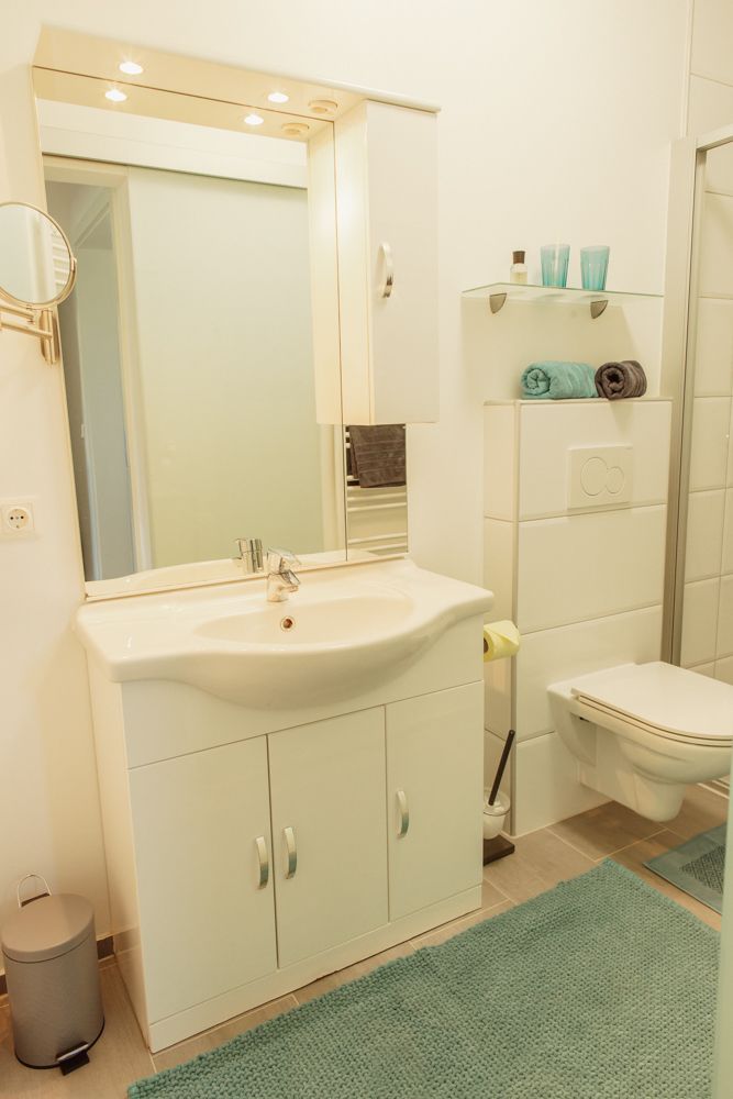 Modernes Badezimmer mit Waschbecken, Spiegel, Toilette und Regalen.