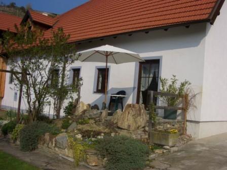 Ein weißes Haus mit rotem Dach, Garten und Sonnenschirm.