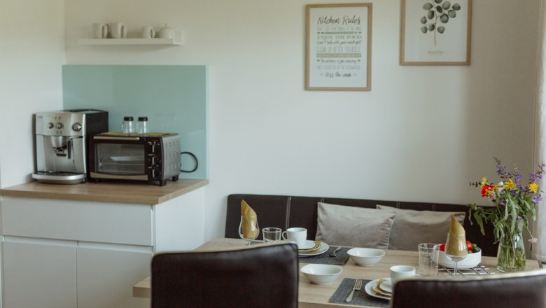 Small kitchen with coffee machine, oven, dining table and flowers.