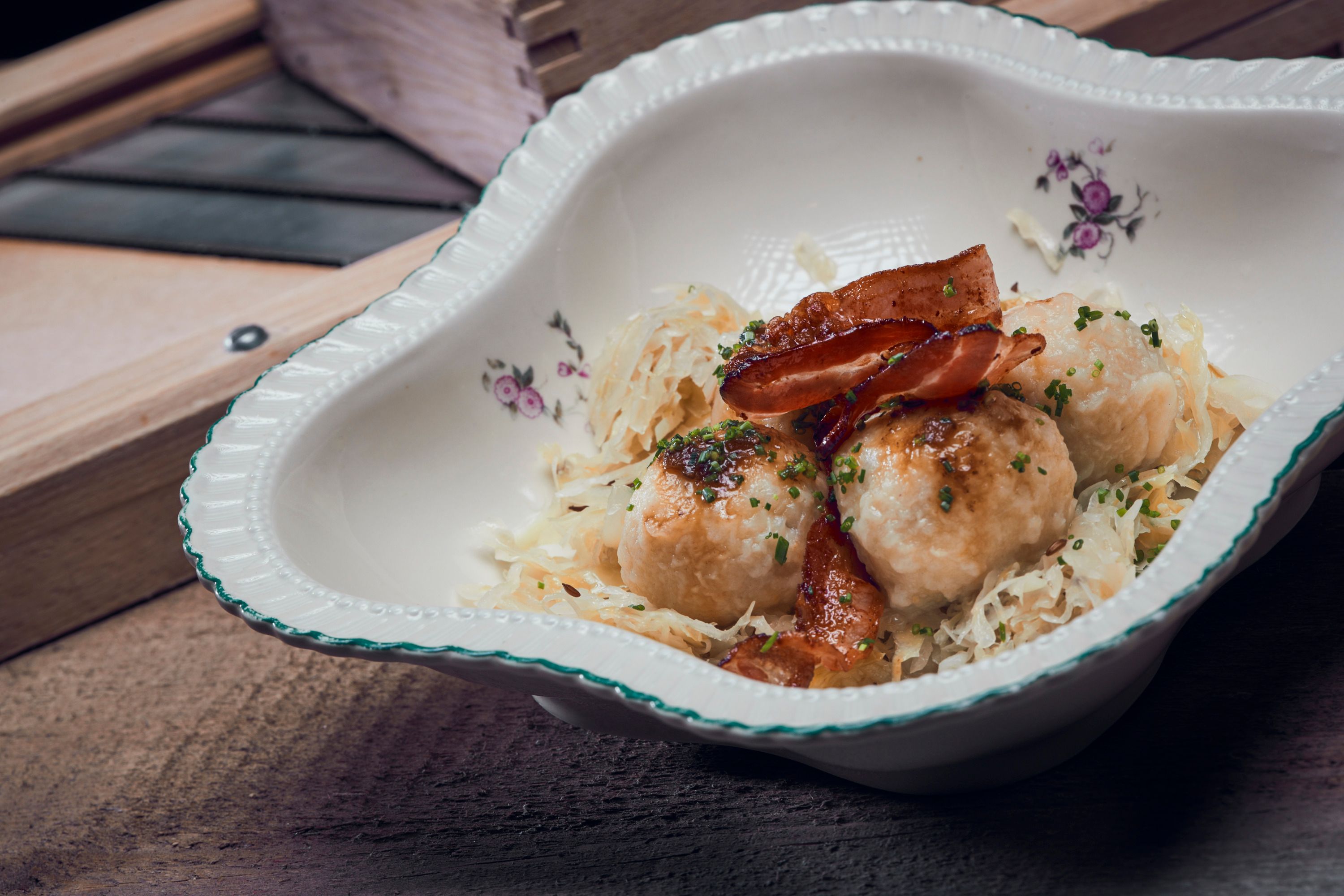 Traditionelles Gericht mit Knödeln, Speck und Sauerkraut in dekorativer Schale.