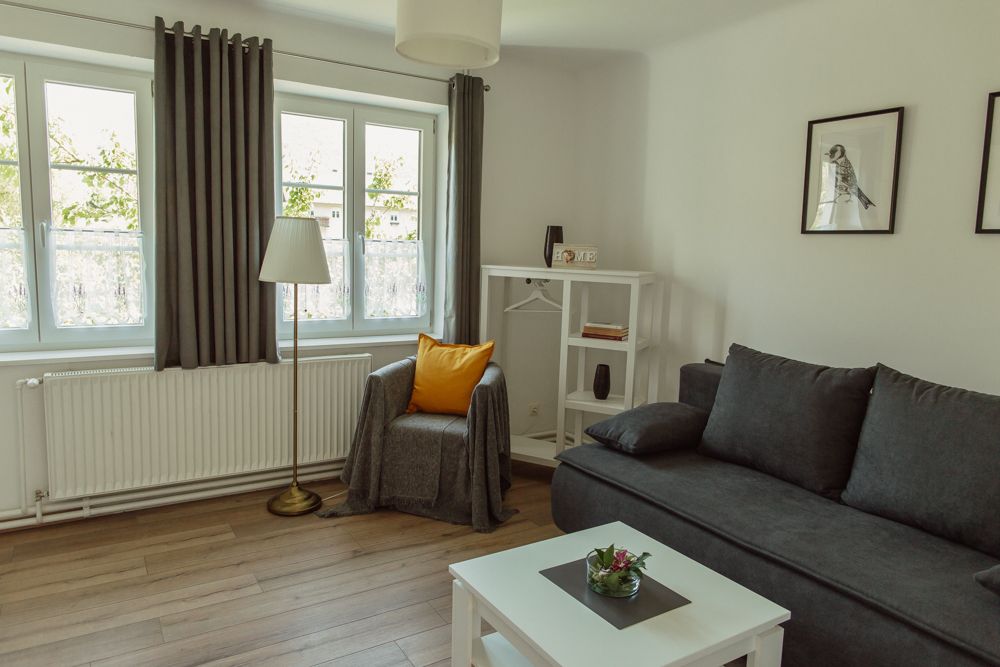 Helles Wohnzimmer mit grauem Sofa, Sessel, Stehlampe und weißen Möbeln.