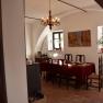 A dining room with a table set with a red tablecloth. A painting hangs on the wall and a chandelier hangs from the ceiling.