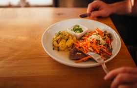 Teller mit Fleisch, Karotten, Kartoffeln und Dip auf Holztisch.