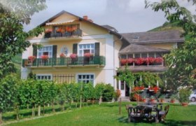 Ein zweistöckiges Haus mit Balkonen und blühenden Blumen, umgeben von einem gepflegten Garten und Weinreben.