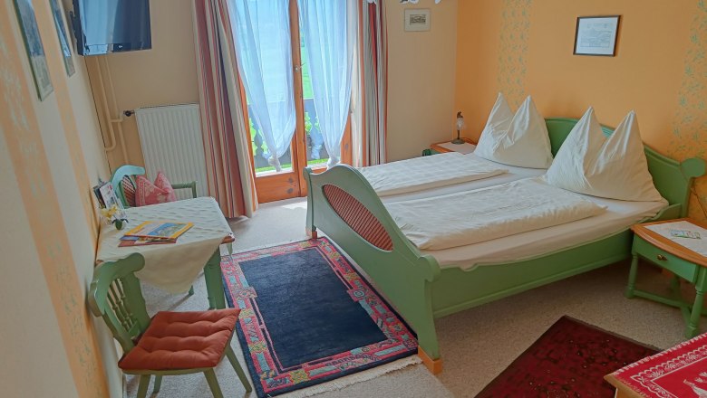 Room with green double bed and table with chair