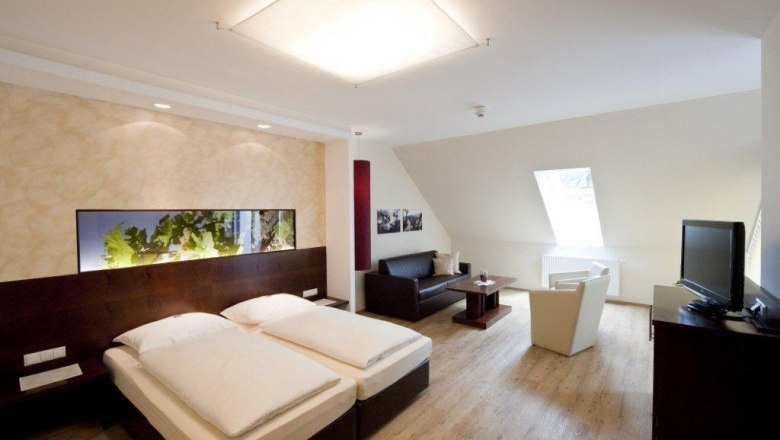 Modernly furnished hotel room with double bed, sofa, armchair and TV.