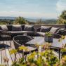 Terrasse mit Sitzmöbeln und Pflanzen, im Hintergrund eine weite Landschaft.