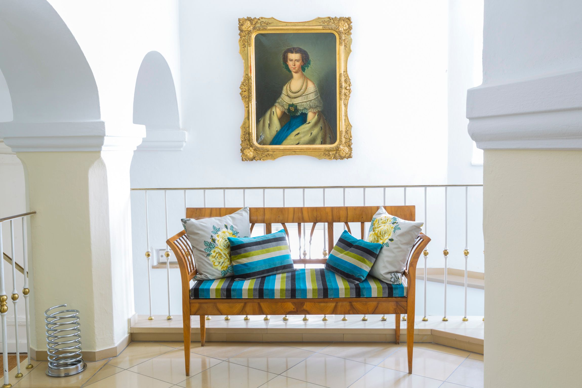 Elegante Sitzbank mit bunten Kissen vor einem Gemälde in einem hellen Raum.
