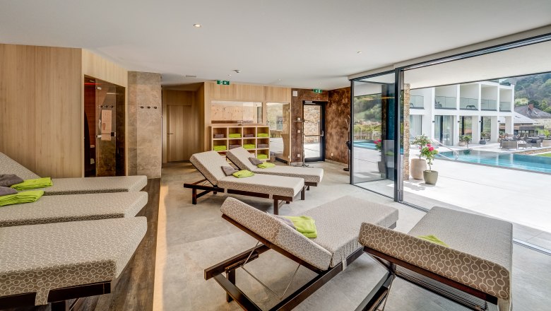 Modern relaxation area with loungers and a view of a pool through large windows.