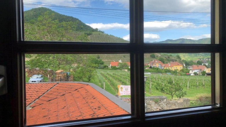 Blick aus einem Fenster auf eine ländliche Landschaft mit Weinbergen, Häusern und einem Hügel im Hintergrund.