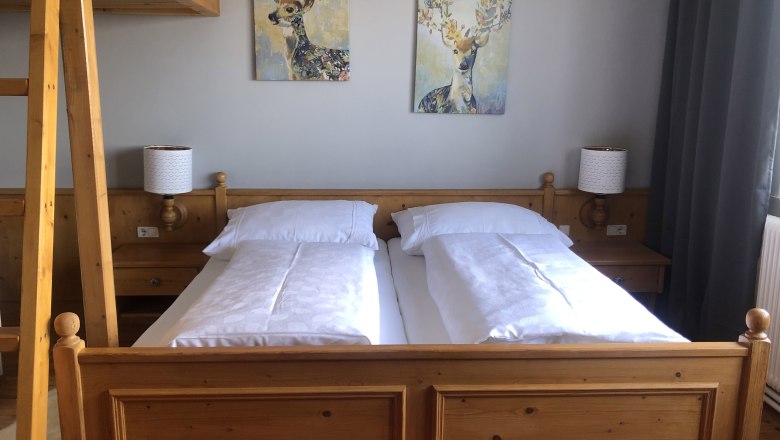 Cozy bedroom with wooden furniture, double bed, two deer paintings on the wall and a ladder to a loft bed.