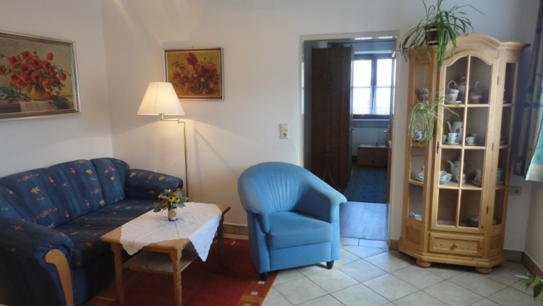 Wohnzimmer mit blauer Couch, blauem Sessel, Holztisch und Vitrine.