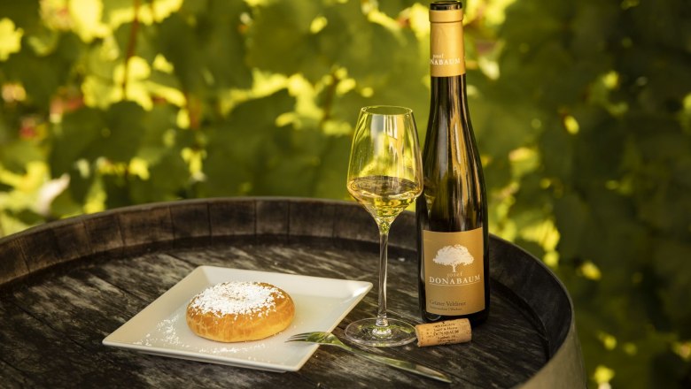 Wine bottle and glass with pastries on a barrel outside.