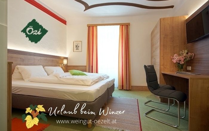 Cozy guest room with double bed, desk and chair, decorated with flowers. Light-colored curtains and carpeted floor.