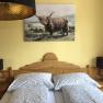 Cozy bedroom with wooden furniture, double bed and picture of a highland cattle on the wall.