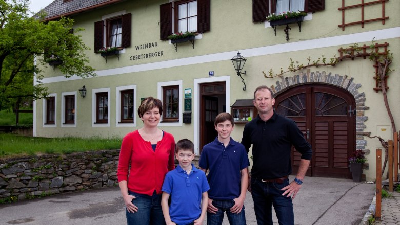Eine Familie steht vor einem Gebäude mit der Aufschrift 'Weinbau Gebetsberger'.