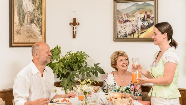 Three people at breakfast, a woman serves orange juice.