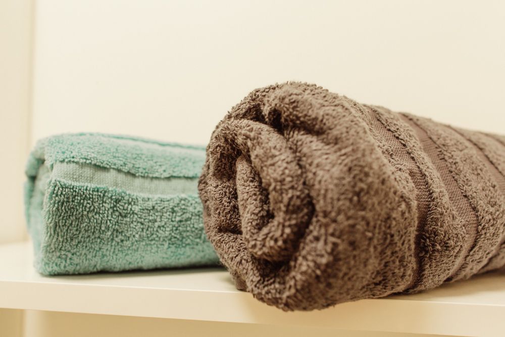 Zwei Handtücher, eines türkis und eines braun, liegen auf einem Regal.