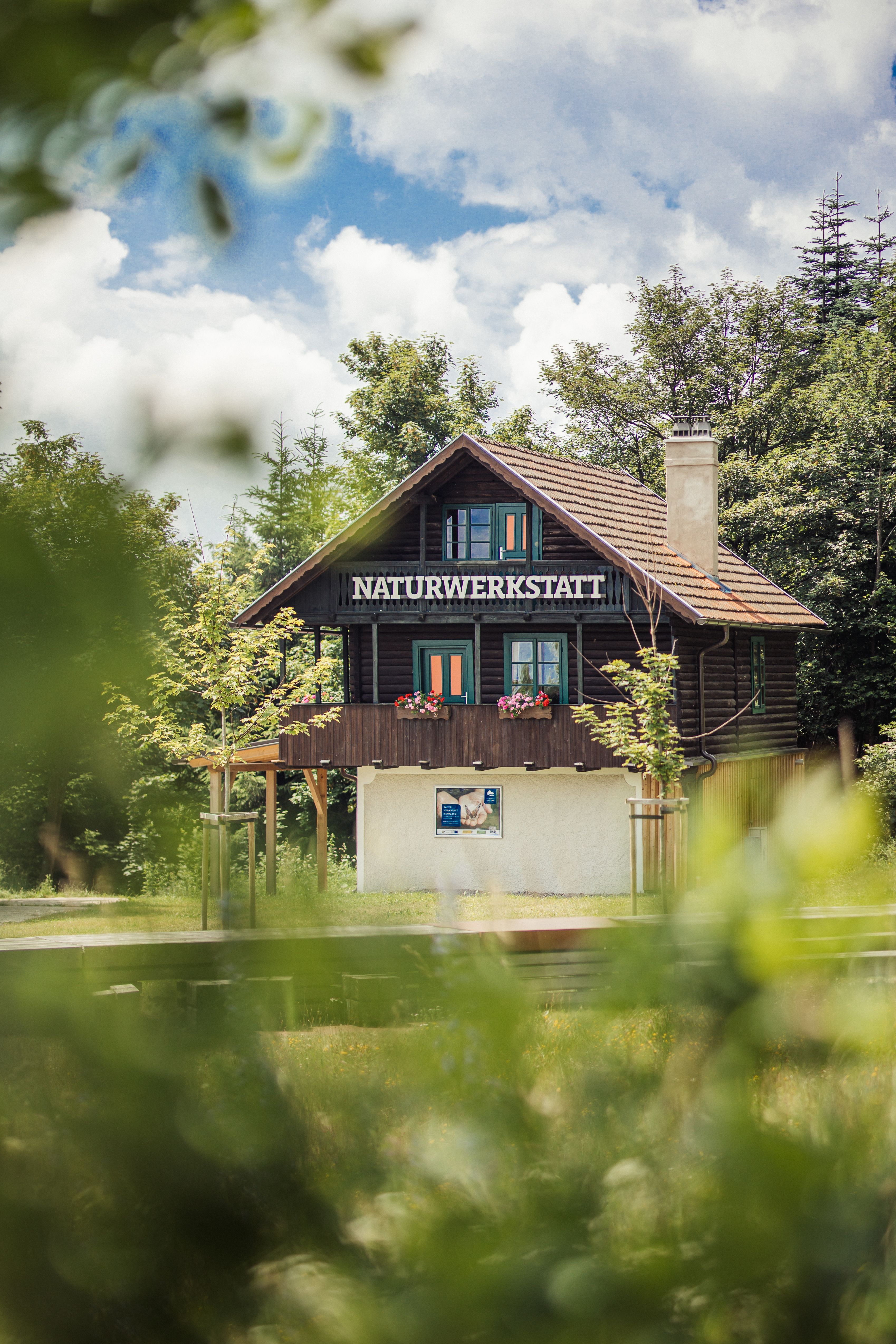Ein idyllisches Haus neben einem Wald mit der Aufschrift Naturwerkstatt.