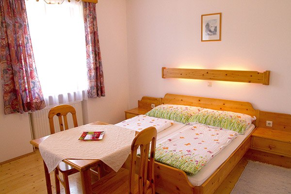 Gemütliches Schlafzimmer mit Holzmöbeln, Doppelbett und kleinem Tisch.