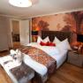 Elegant suite with large bed, decorative cushions and stylish wallpaper in Luberegg Castle.