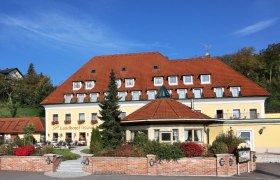 Außenansicht eines gelben Landhotels mit rotem Dach und Garten.