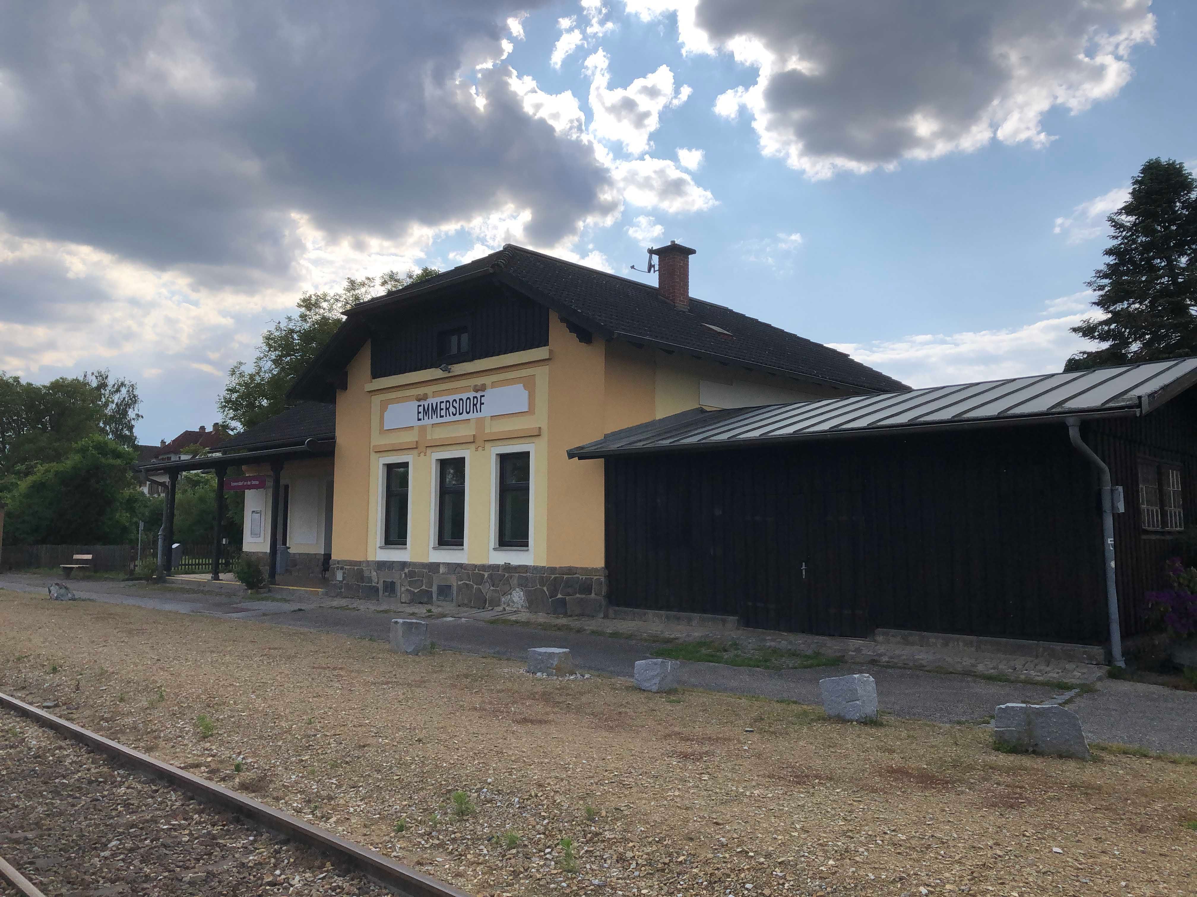 Bahnhof Emmersdorf mit gelbem Gebäude und Gleisen im Vordergrund.