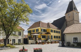 Idyllic village square with inn and terrace and a church tower in the background.