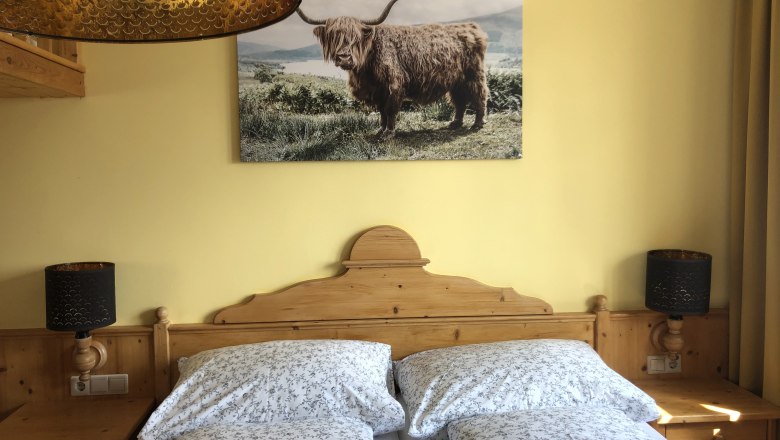 Cozy bedroom with wooden furniture, double bed and picture of a highland cattle on the wall.
