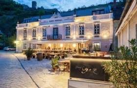 Außenansicht des Gasthofs Prankl bei Abenddämmerung mit beleuchteter Terrasse und Burg im Hintergrund.