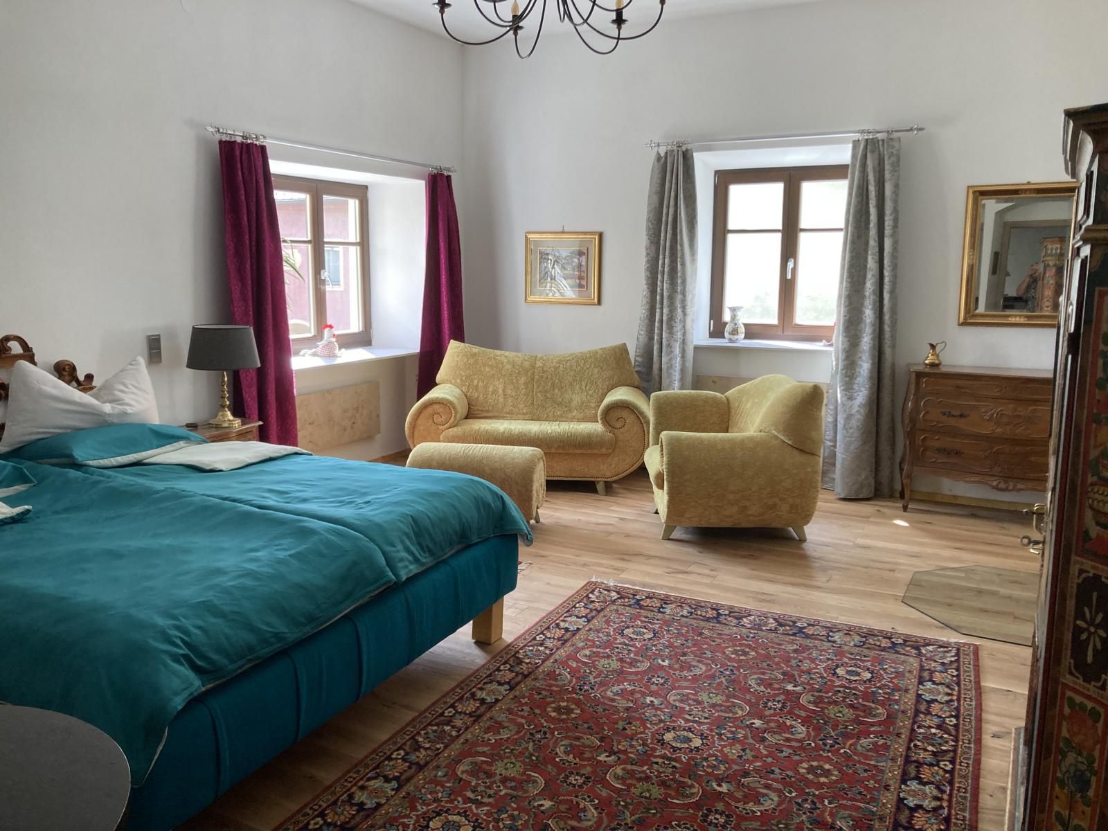 Gemütliches Schlafzimmer mit blauem Bett, gelben Sesseln, Teppich und Holzmöbeln.