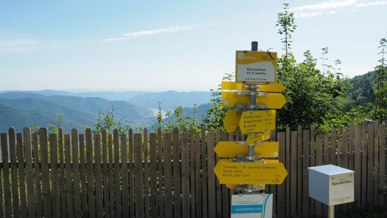 Signpost on the Jauerling with a view of wooded hills and blue sky.