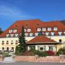 Exterior view of a yellow country hotel with a red roof and garden.