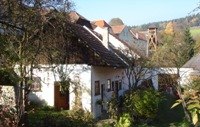 Ein ländliches Gebäude mit weißen Wänden und roten Ziegeldächern, umgeben von Bäumen und Büschen.