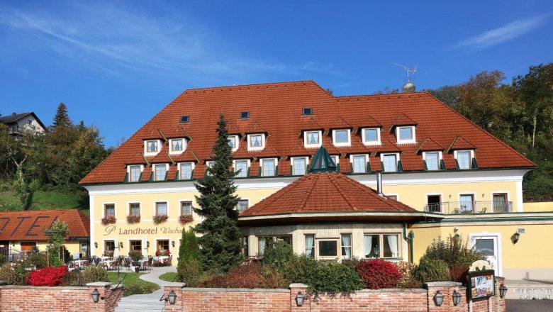 Außenansicht eines gelben Landhotels mit rotem Dach und Garten.