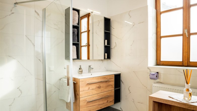 Modern bathroom with wooden furniture, large window front and glass shower.