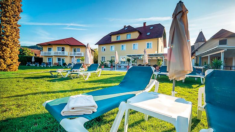 Sun loungers on a lawn in front of a yellow hotel building in the sunshine.