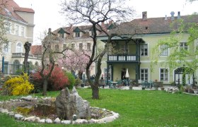 Ein Garten mit Teich und Bäumen vor einem historischen Gebäude mit Balkon.