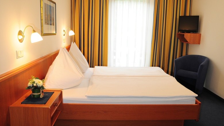 Ein Hotelzimmer mit Doppelbett, blauen Vorhängen und einem kleinen Fernseher an der Wand.
