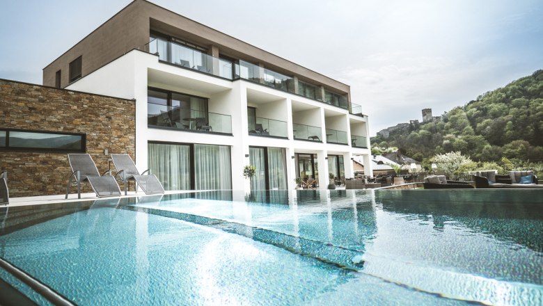 Modernes Boutiquehotel mit Pool und Liegestühlen, umgeben von grüner Landschaft.