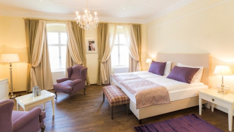 Barock-Landhof Burkhardt, © Burkhardt Elegantes Schlafzimmer mit Doppelbett, lila Akzenten und Kronleuchter.