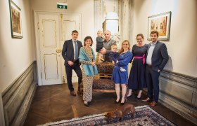 A group of people pose in an elegant room with a dog in the foreground.