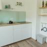 Modern kitchen with white cupboards, glass splashback and wooden shelves.